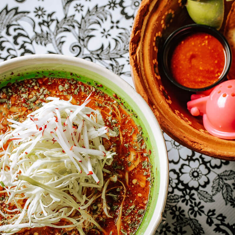 A bowl of Pozole in a white and green bowl.